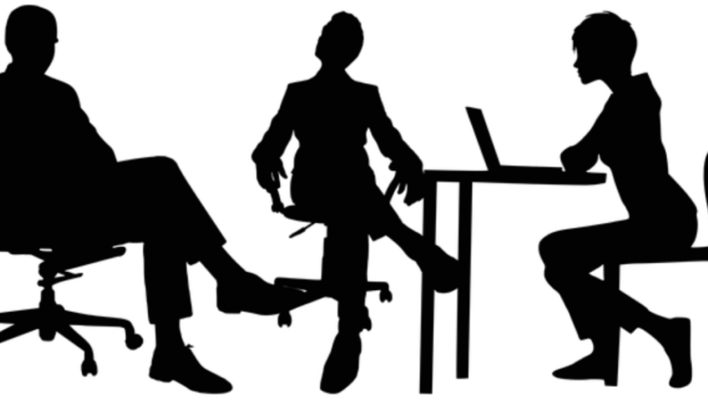 A group of professionals conducting an interview in a modern office setting, with one candidate being interviewed by a panel of interviewers. The image conveys a formal and professional atmosphere, highlighting the interview process at Concentric Advisors.